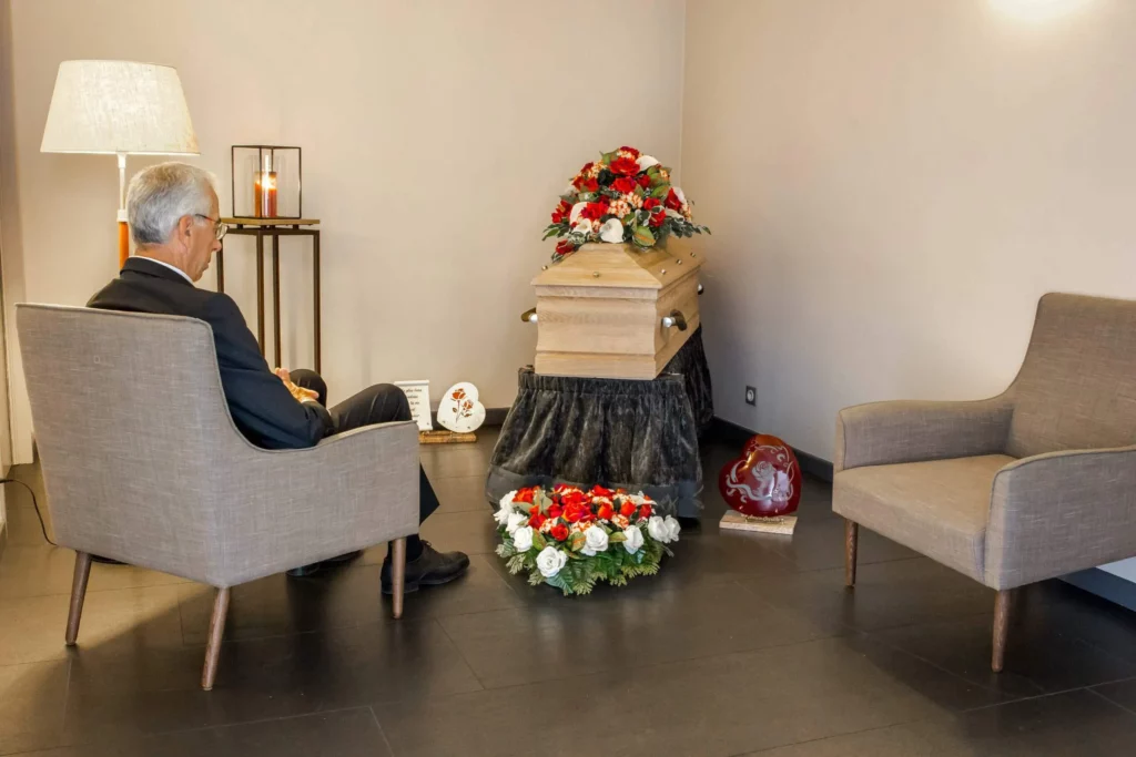 Homme en recueillement dans un salon funéraire devant un cercueil fleuri.