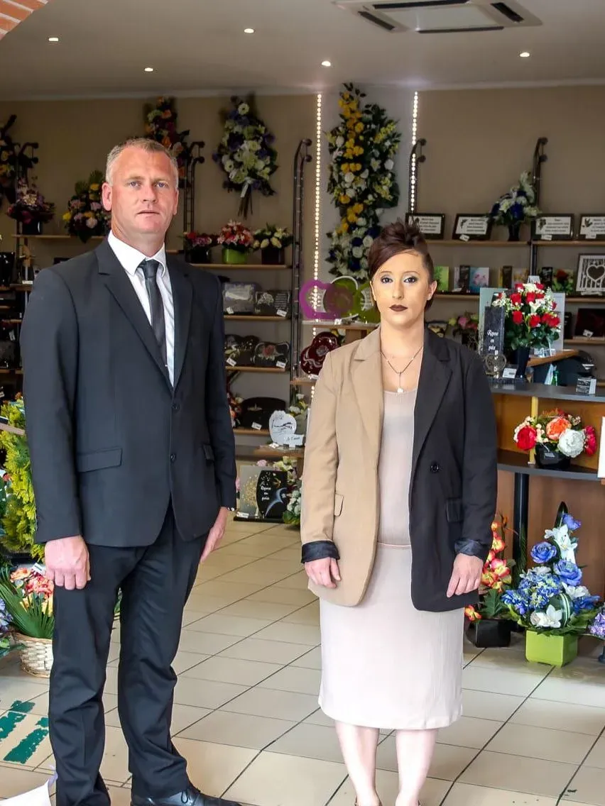 Deux agents funéraires en tenue professionnelle dans le magasin d'articles d'obsèques.