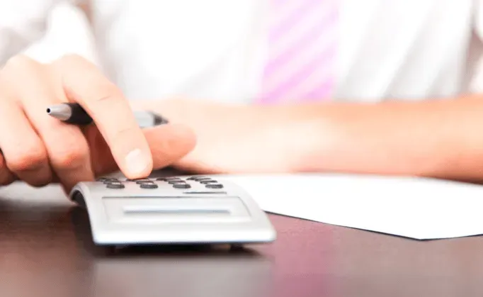 Personne calculant les frais d'un devis d'obsèques sur une calculatrice.